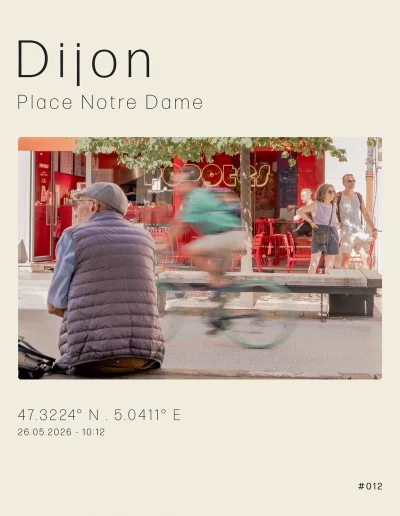 Vue sur une personne âgée, assise sur un banc, place Notre Dame. Un cycliste traverse la scène. Au troisième plan, la vitrine du restaurant Popotes et des touriste qui contemplent l'église Notre Dame de Dijon.