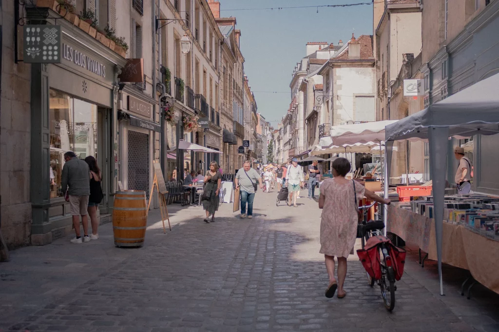 Vue sur des passants et des commerçants de la rue Musette par une belle matinée d'été.