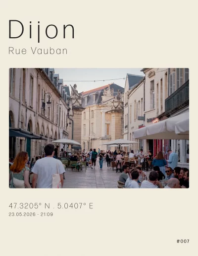 Vue de la rue Vauban, en direction de la place de la Libération. Les terrasses de la ruelle piétonne sont remplies, quelques passants passent entre les tables et les chaises. Tout au fond, vue sur l'aile droite du Palais des Ducs de Bourgogne.