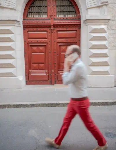 Homme en pantalon rouge passant devant une grande porte rouge à Dijon