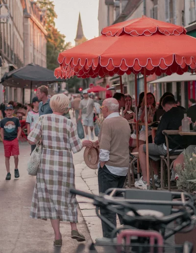 Passants et clients en terrasse sous de grands parasols rouges dans une rue de Dijon